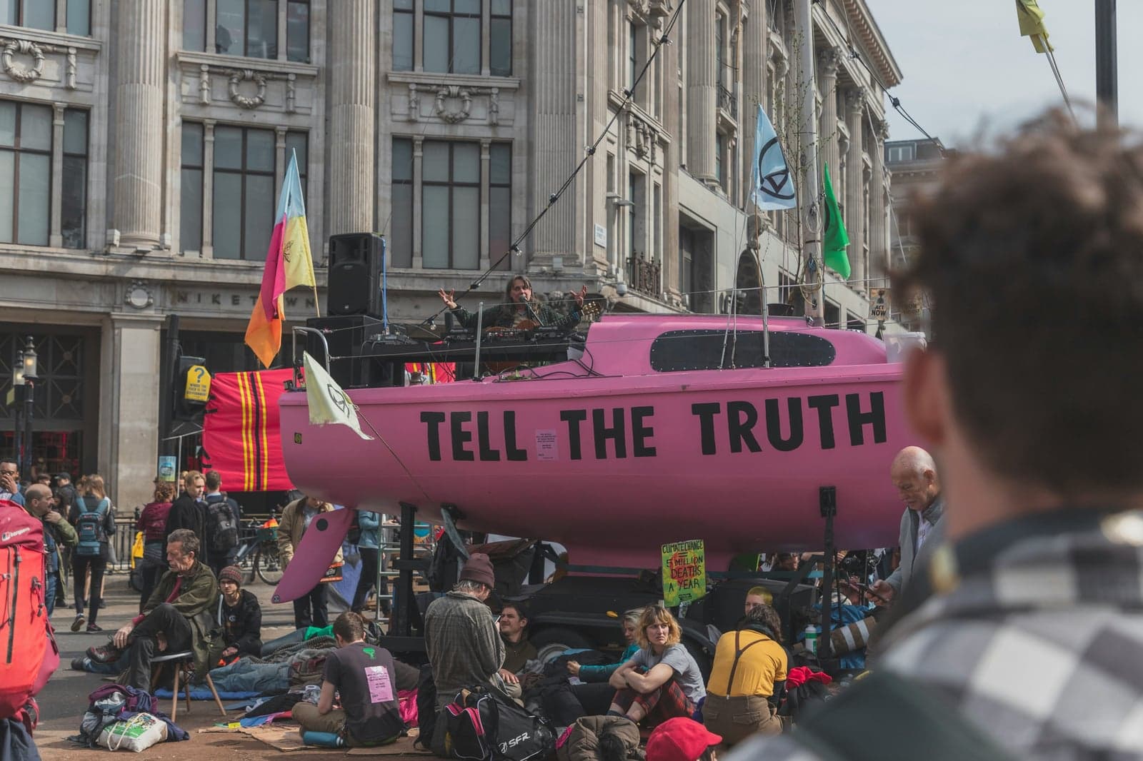 Picture of a rally in the middle of the road and a float with a sign that says "tell the truth"