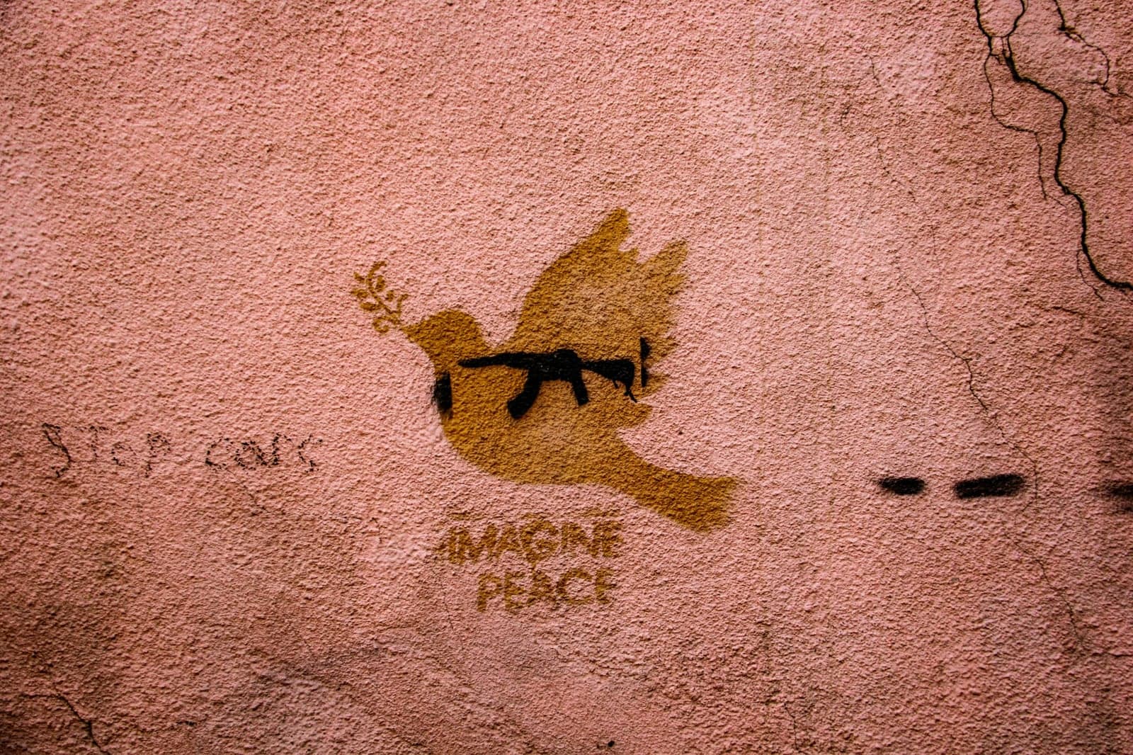 Street art representing the dove of peace (colored gold) with a black rifle gun drawn inside it along with the phrase "imagine peace"